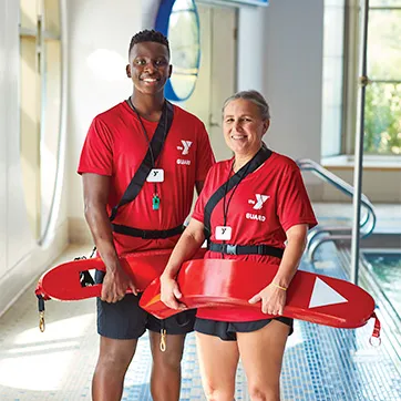 one male and one female lifeguard standing by a pool smiling at the camera