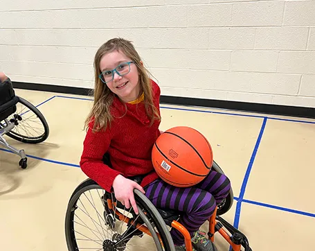 Young girl sitting in wheelchair holding a basketball