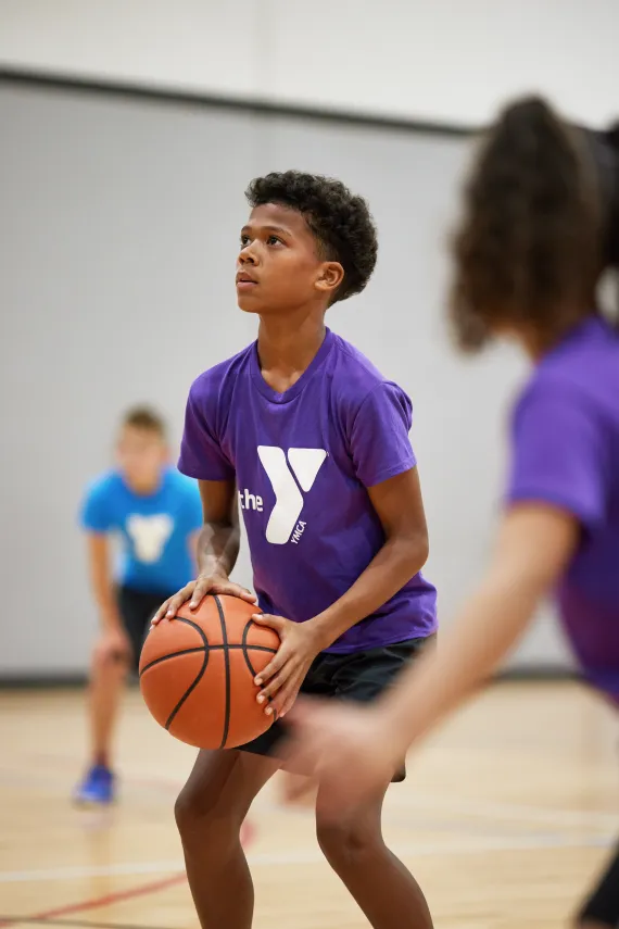 A teenage boy focuses at the indoor basketball game as he lines up his shot.