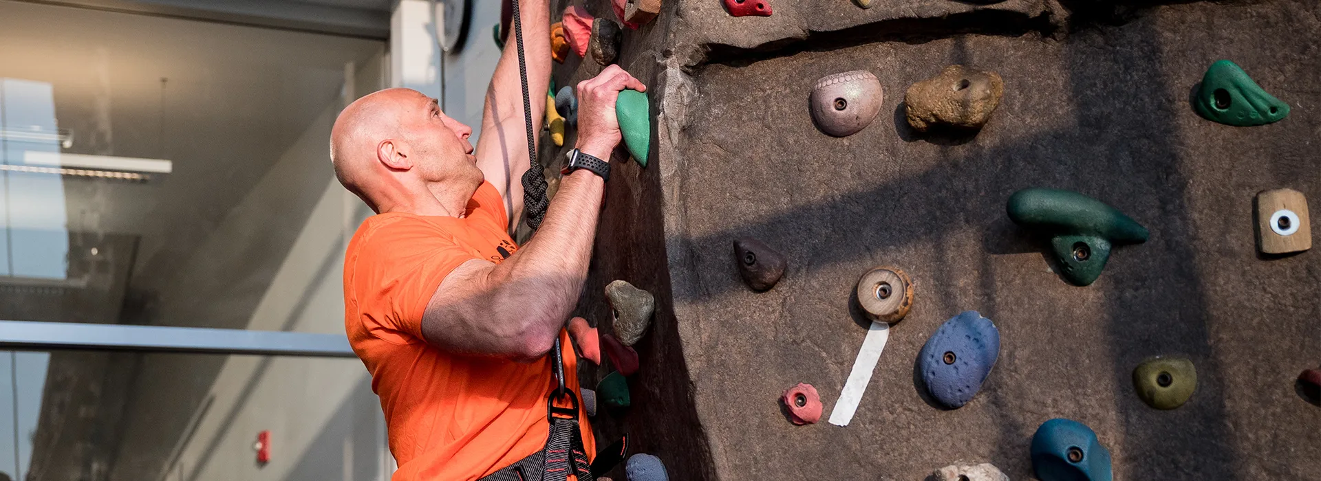 man wearing orange shirt climbing wall