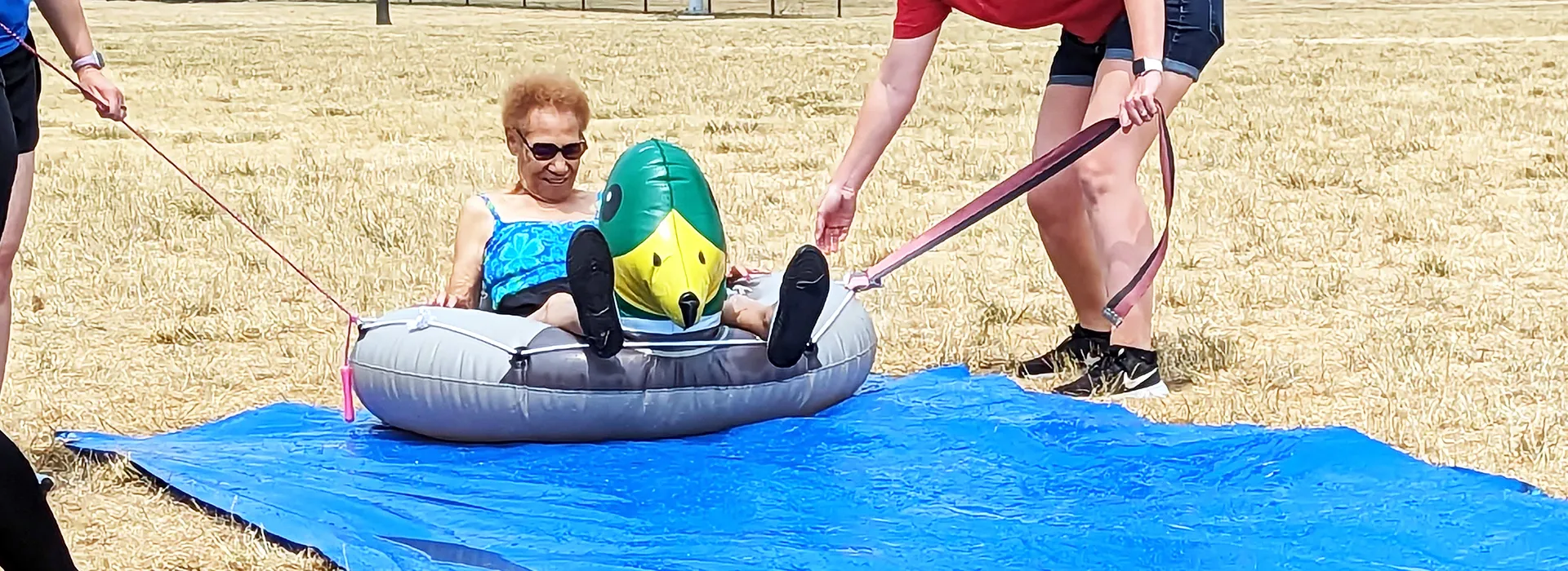 woman sitting in a duck pool float being pulled down a large blue tarp